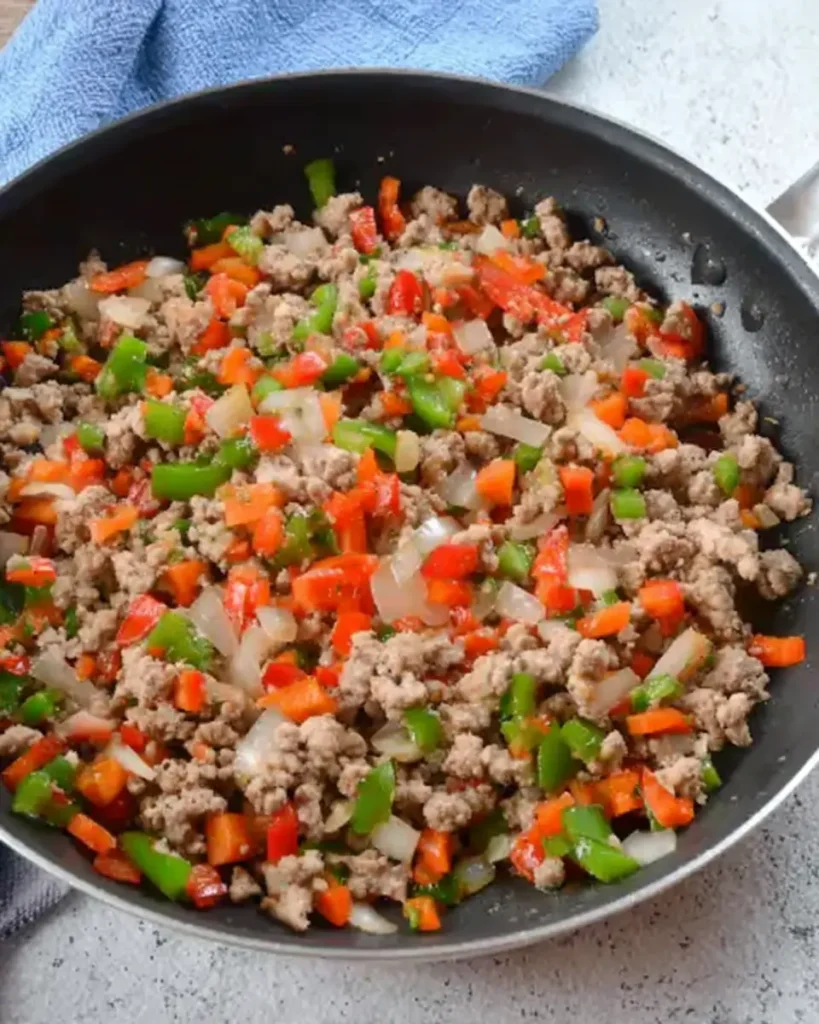 Breakfast burrito filling—browned sausage with peppers and onions—sizzling in a nonstick skillet