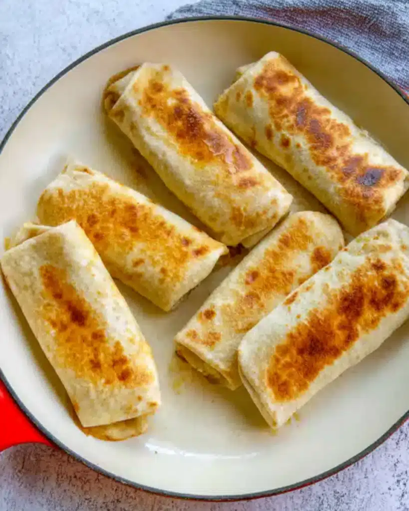 Breakfast burritos searing seam-side down in a white skillet until golden and crispy