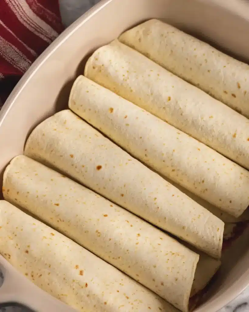 The Best Ground Beef Enchiladas Recipe Everyone Will Love 3 Rolled tortillas arranged in a baking dish for ground beef enchiladas